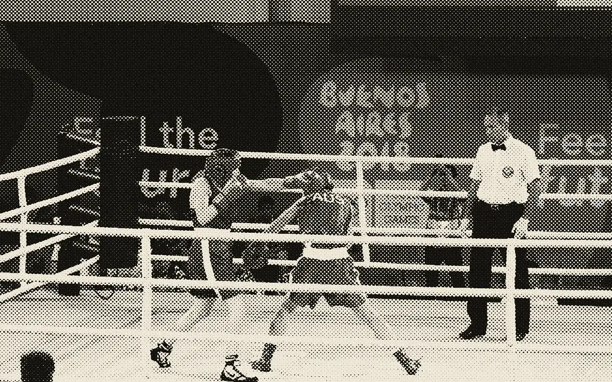 Deux boxeuses casquées échangent des coups sur un ring de tournoi, sous le regard de l'arbitre en chemise blanche